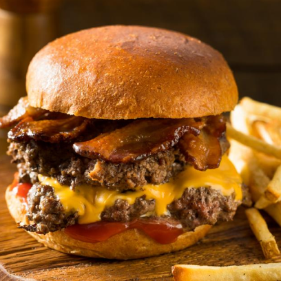 Um hambúrguer suculento com bacon, queijo derretido e tomate, servido ao lado de batatas fritas em uma tábua de madeira.