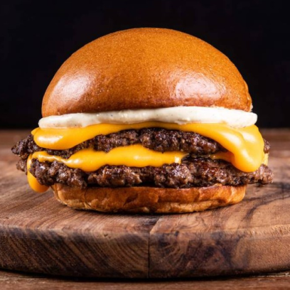 Um hambúrguer suculento com bacon, queijo derretido e tomate, servido ao lado de batatas fritas em uma tábua de madeira.