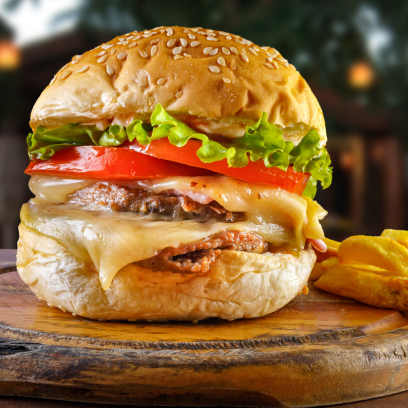 Uma imagem de um hambúrguer com um bolinho de peixe, alface, tomate, cebola e picles em um pão com gergelim, servido em uma tábua de madeira com uma tigela pequena de maionese ao lado.