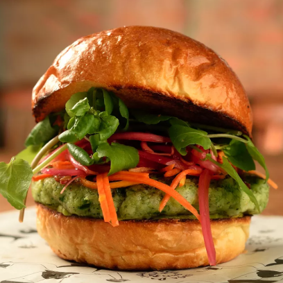 Pão liso, hamburguer vegano de 160g de cor verde, alface, cenoura e tomate ralados.